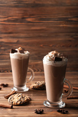 Glass cups of tasty cocoa drink with cream and sweets on wooden table