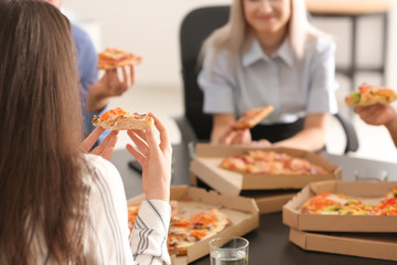 Young people eating pizza at table in office