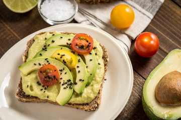 Avocado Spread and Slices with Cherry Tomato and Black Sesame on Wooden Background as Vegetarian Food Concept