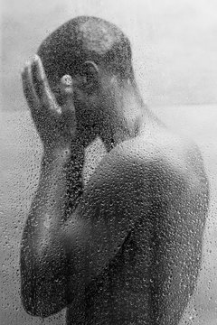 side view of young african american man washing body in shower, black and white photo