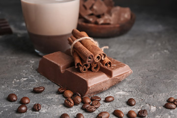 Chocolate piece with cinnamon sticks and coffee beans on textured background