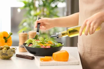 Fototapeten Woman dressing fresh vegetable salad with olive oil in kitchen © Pixel-Shot