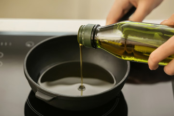 Woman pouring olive oil into frying pan on stove