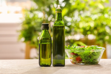 Bottles with olive oil and vegetable salad on table against blurred background
