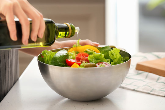 Woman Dressing Fresh Vegetable Salad With Olive Oil In Kitchen