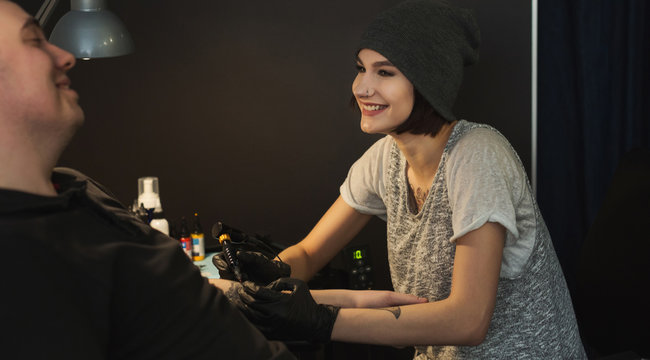 Young woman tattooist doing tattoo on male arm