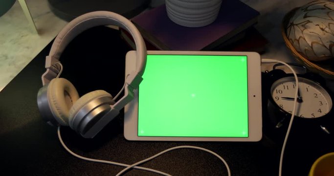 Dolly shoot of Green Screen on Digital tablet and headphones on desk at night,