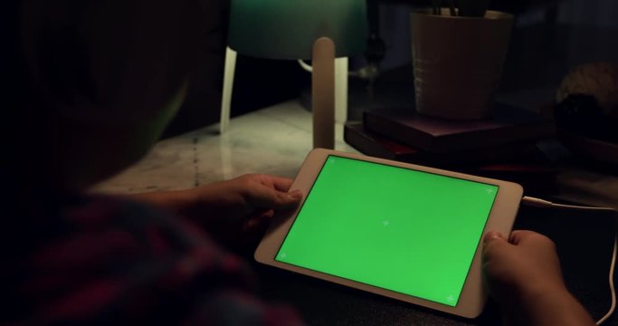 Over the shoulder view of asian boy using tablet computer with headphone, Green screen of technology being used. Chroma Key tablet.