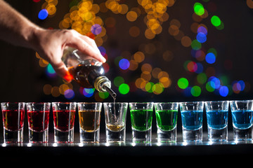 Bartender pouring alcoholic drink into small glasses on bar. Colorful cocktails at the bar.