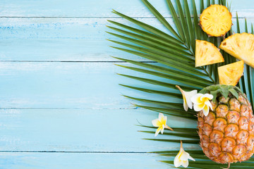 Summer vacation background concept. Pineapples and  palm branch on wood plank blue color. Top view, copy space