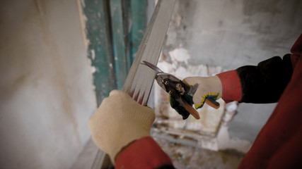 Construction worker uses metall cutting scissors to cut metall drywall profiles.