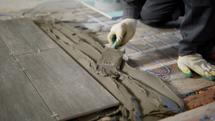 close up shot of the builder hands in gloves, who puts the cement mixture on the brick floor to create a glue under the tile