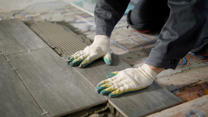 tiler is installing ceramic floor tiles above cement and electric floor heating, aligning, using...