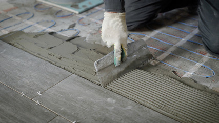 Anonymous site worker applying cement on floor and laying tiles