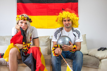 Weiblicher und männlicher Fan der deutschen Nationalmannschaft auf Couch frustriert
