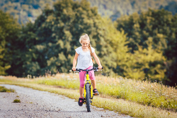 Fototapeta premium Girl on bicycle cycling down a dirt path in summer, woods in the background