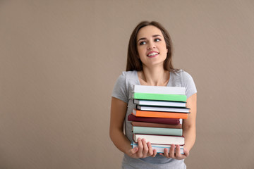 Young woman with stack of books on color background