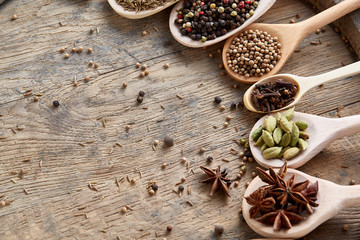 Spoons with aromatic various spices for cooking on old wooden board, close-up, flat lay, selective focus.