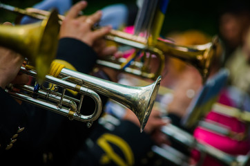 An orchestra in black uniform playing trumpets outdoors. Musical instruments closeup with blurred...