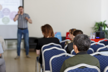 Spectators listen to the speech in the conference room. The focus is under the person on the front surface