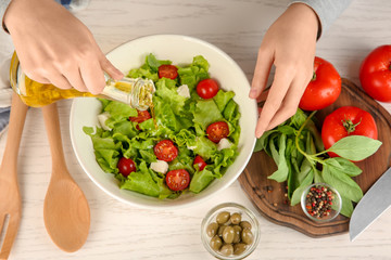 Woman adding olive oil into bowl with fresh vegetable salad on table