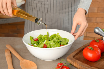 Woman adding olive oil into bowl with fresh vegetable salad on table