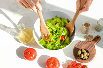 Woman preparing tasty vegetable salad on table