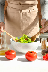 Woman preparing tasty vegetable salad on table
