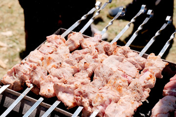 Preparation of shish kebab on skewers. Pieces of meat strung on metal sticks are prepared on hot coals. People in summer cook food on the street.
