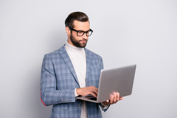 Portrait of half turned, virile, harsh, attractive, intelligent, stunning man in glasses having laptop in hands, checking email, using wifi internet, standing over gray background