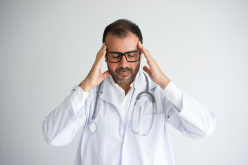 Portrait of frustrated medical worker holding head in hands. Mid adult Caucasian male doctor...