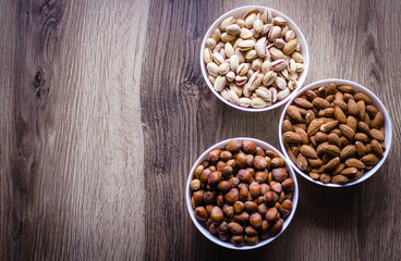 Mixed nuts in a white ceramic bowl on a wooden background.