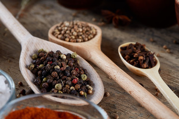 Various spices in wooden spoons and bowls and some salt on an old wooden barrel, top view, close-up, selective focus.