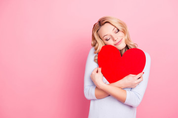 Portrait with copy space empty place of  dreamy pretty girl hugging big red carton heart figure with crossed hands, close eyes isolated on pink background
