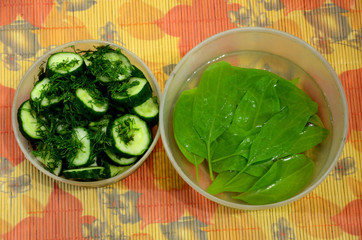 
Two plastic bowls-one with sliced ​​cucumber with dill, the second with spinach in the water.