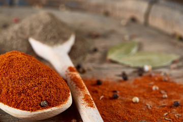 Top view of a wooden spoons full of paprica and black pepper on wooden barrel background, selective focus.
