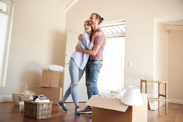 Happy Couple Surrounded By Boxes In New Home On Moving Day