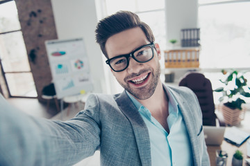 Self portrait of joyful funny man in shirt and jacket making selfie on smart phone with hand,...