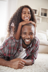 Portrait Of Daughter Lying On Fathers Back In Lounge