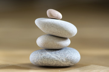 Fototapeta na wymiar Group of zen stones pile, grey meditation pebbles tower on light brown wooden background in sunlight