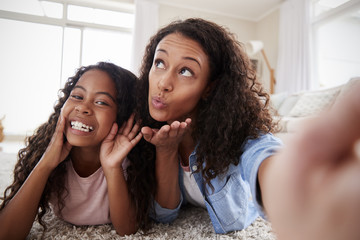 Mother And Daughter Lying On Rug And Posing For Selfie At Home
