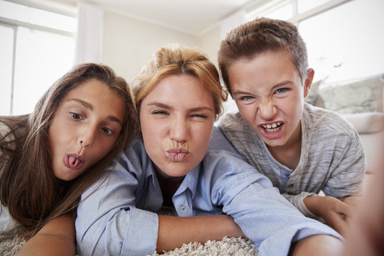 Mother And Children Lying On Rug And Posing For Selfie At Home