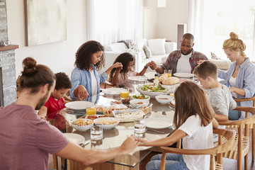 Two Families Praying Before Enjoying Meal At Home Together