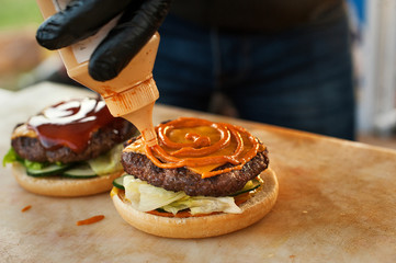 The chef prepares a burger in the open air kitchen. Dripping mustard. Street fast food.