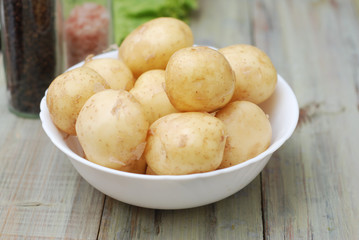 New Raw Potatoes in Bowl on Rustic Wooden table. Close up view, Wooden Spoons, over Wooden Background.