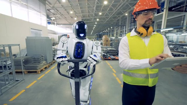 Human-like robot is pulling a factory transporter while walking together with a factory worker