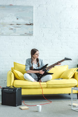 beautiful teen girl playing electric guitar on sofa in living room