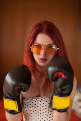 pretty young woman with red hair, sunglasses and boxing gloves looks upset, feminism, self defense concept 