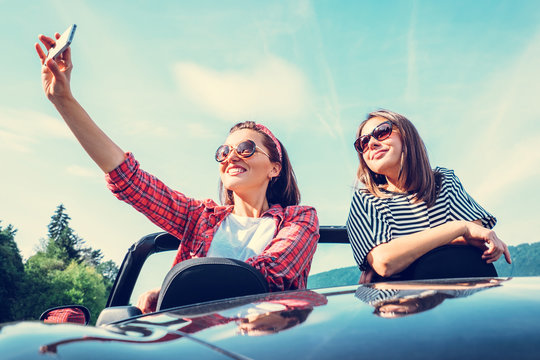 Two female freinds take a selfie photo in cabriolet car during their summer voyage