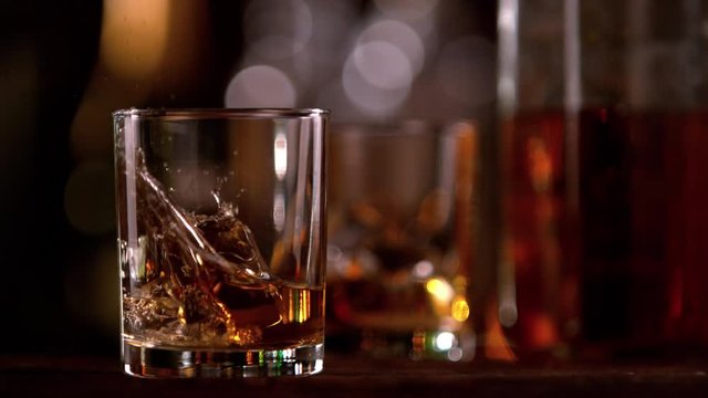 Super slow motion of falling ice cube into whiskey glass. Filmed on cinema slow motion camera, 1000fps